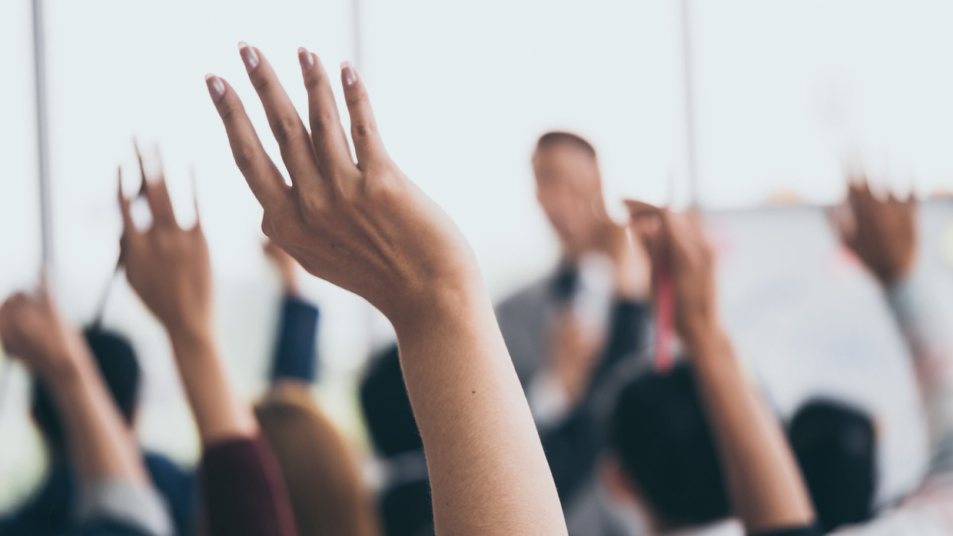 Staff training: Audience raising hands up while businessman is speaking in training at the office.